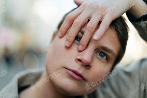 Preview: Young person covering one eye with hand in city street