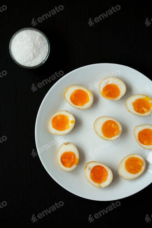 Preview: Homemade Unami Soy Sauce Eggs on a white plate on a black background, top view.