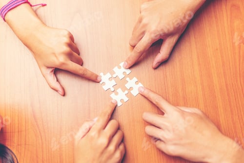 Preview: High Angle View Of Businesspeople Hand Solving Jigsaw Puzzle On Wooden Desk