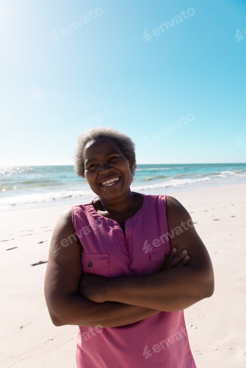 Preview: Cheerful african american senior woman with arms crossed standing against scenic view of sea and sky