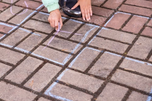 Preview: girl draws a hopscotch with chalk on the pavement.Child playing the game outside. Kid wearing