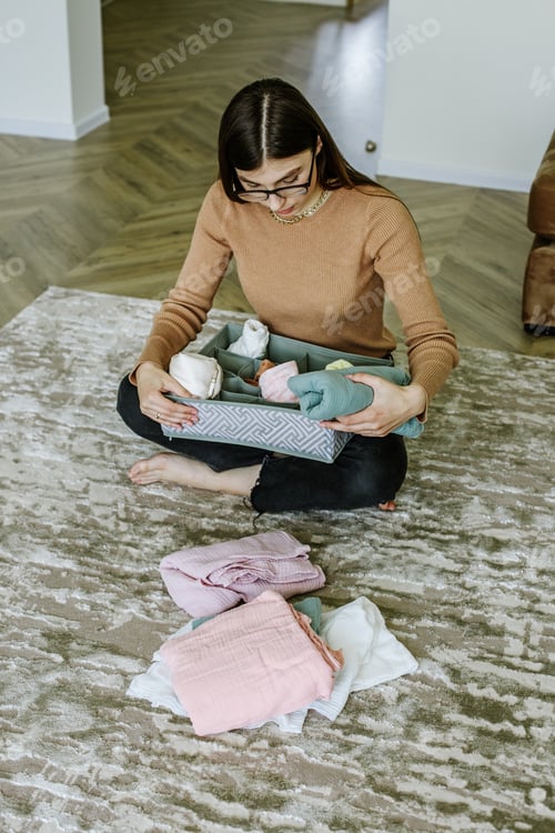 Preview: Young hostess neatly folds children's clothes into an organizer box according to Marie Kondo method