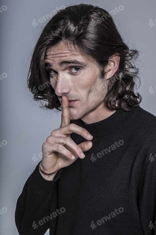 Preview: Portrait of a long-haired boy making a silent gesture in front of a gray background.