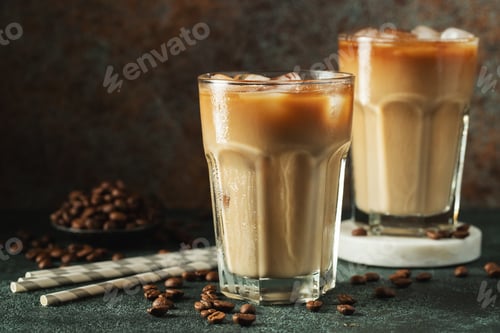 Preview: Ice coffee in a tall glass with cream poured over, ice cubes and beans on a dark concrete table.
