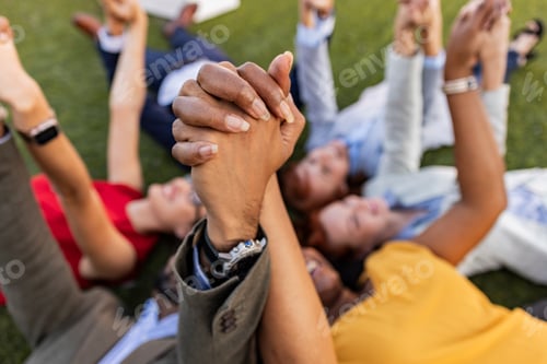 Preview: Group of business people holding hands lying on grass