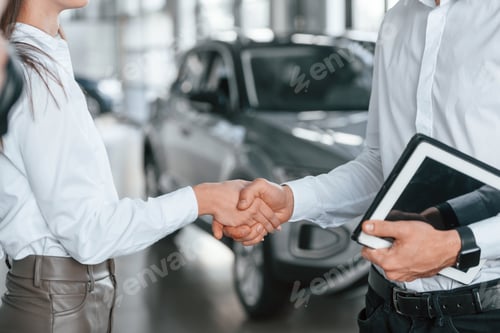 Preview: Doing handshake. Close up view. Man with woman in white clothes are in the car dealership together