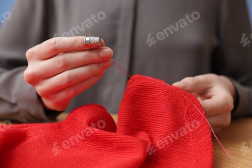 Preview: Woman sewing cloth with thread at wooden table, closeup