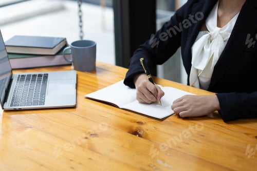 Preview: Attractive young businesswoman secretary in office working laptop writing work schedule on notepad.