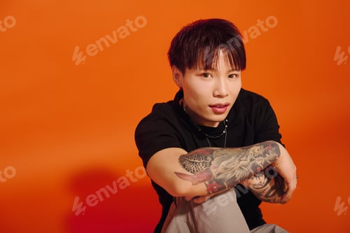 Preview: Stylish young man poses confidently against vibrant orange backdrop showcasing modern fashion