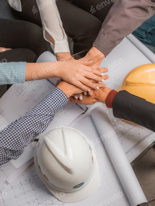 Preview: Vertical shot of groupmates' hands on top of each other over project documents and helmets