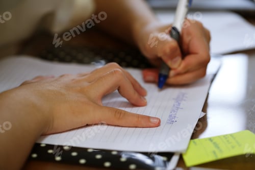 Preview: Student holding pen in hand doing homework closeup on desk blur background