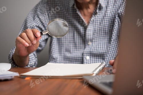 Preview: Asian senior businessman holding magnifying glass check work documents and business reports