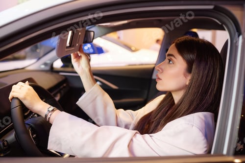 Preview: Female Client Looking in Mirror Choosing Car at Dealership Center
