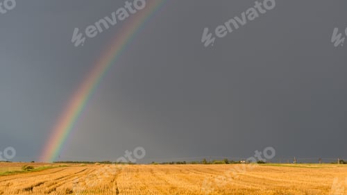 Preview: Rainbow over a field on a hot summer stormy day with a dark sky in the background.