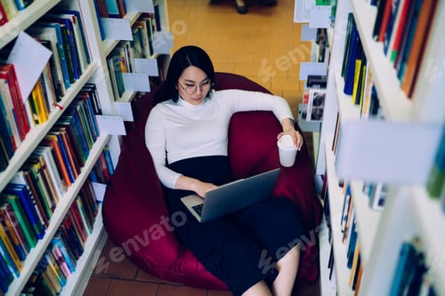 Preview: Young woman using laptop in library