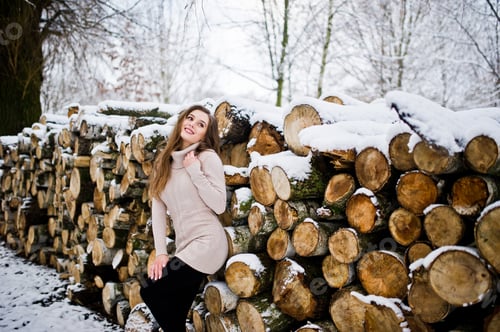 Preview: Beautiful brunette girl in winter warm clothing. Model on winter sweater near stump.