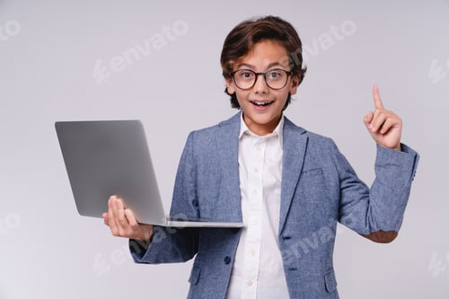Preview: Young small boy in formal outfit having idea holding laptop isolated over grey background