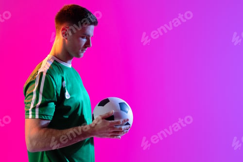 Preview: Caucasian male soccer player with football over neon pink lighting