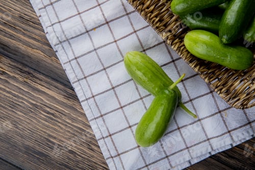 Preview: top view of cucumbers in basket plate with other ones on cloth and wooden background