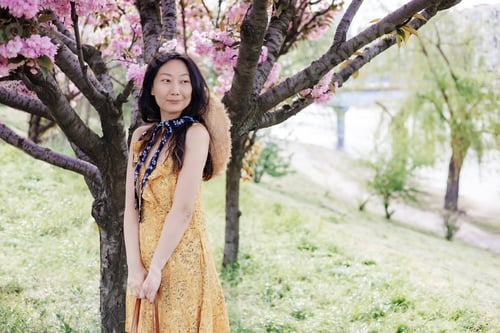 Preview: Happy young Asian woman in a wicker hat walks in a blooming city park. Portrait of a stylish emotion