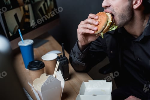 Preview: cropped view of guard eating burger at workplace