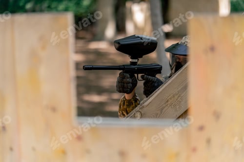 Preview: in the wild crouching near tree structures player in a pintball uniform holds a pistol with a