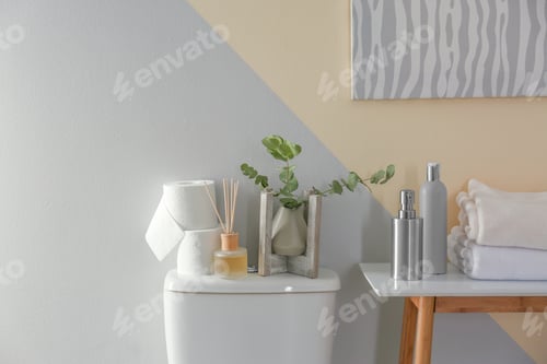 Preview: Table and toilet bowl with decor elements and necessities near color wall. Bathroom interior