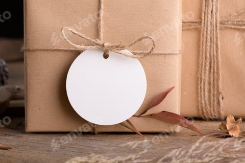 Preview: Round white gift tag mockup on craft wrapped presents on wooden background with boho decoration