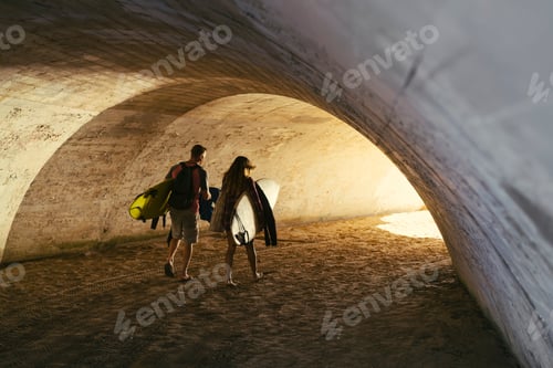 Preview: Rear view of surfing couple walking through beach underpass, Newport Beach, California, USA