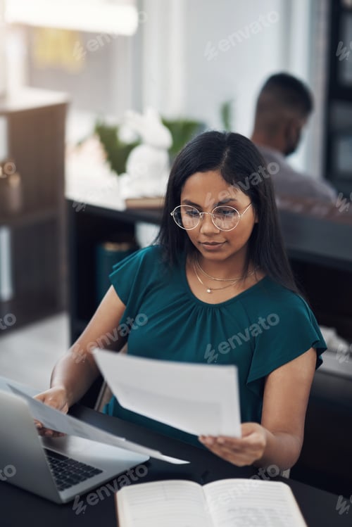 Preview: Shot of a young businesswoman going through paperwork while working in an office