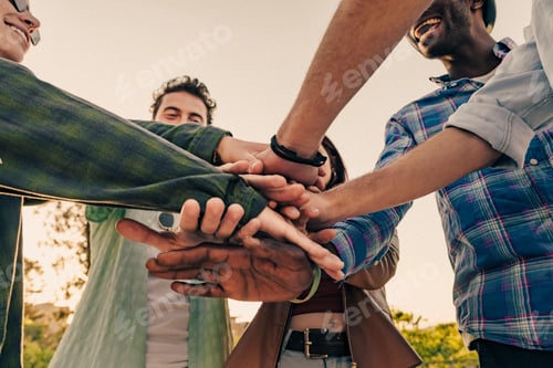 Preview: Teamwork and unity symbolized by diverse group stacking hands together outdoors