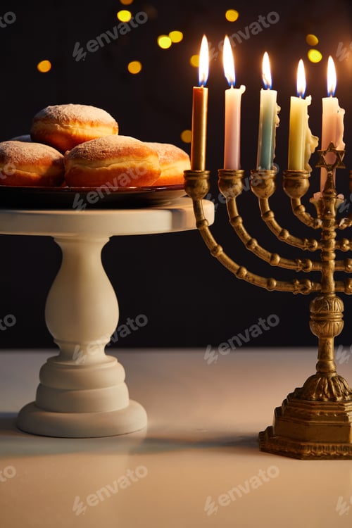 Preview: delicious doughnuts on stand near glowing candles in menorah on black background with bokeh lights