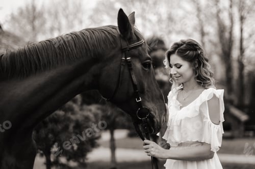 Preview: Beautiful girl in a white sundress next to a horse on an old ranch. black and white photo