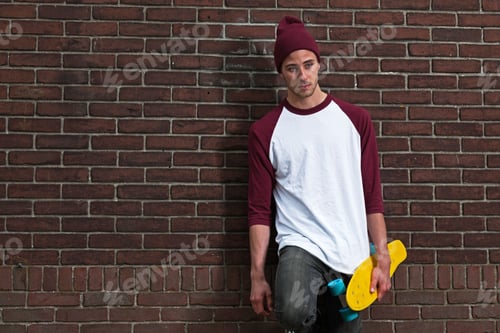 Preview: Hip Cool Urban Fashion Skateboarder With Woolen Hat Posing In Front Of Brick Wall.