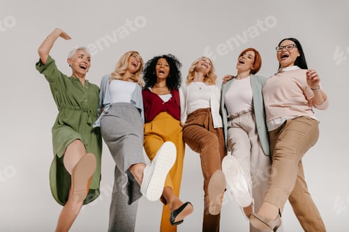 Preview: Multi-ethnic group of happy mature women embracing and dancing against grey background