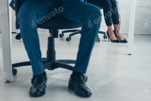 Preview: cropped view of african american businessman sitting in office near colleague suffering from pain in