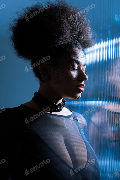 Preview: young african american woman in sexy outfit and black veil near ruffled glass with blue lighting