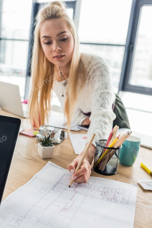 Preview: beautiful female architect working on blueprint in loft office