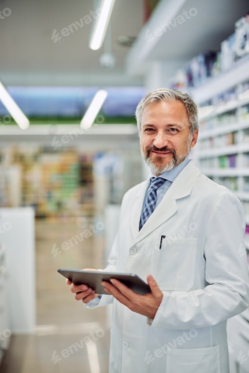 Preview: Portrait of a smiling male pharmacist holding a digital tablet in a workplace.