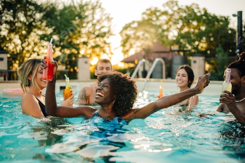 Preview: Friends enjoying drinks and laughing in swimming pool at sunset