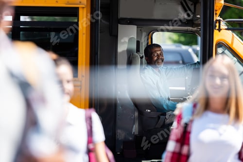 Preview: happy mature school bus driver looking at teenagers walking on foreground