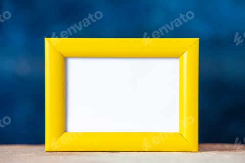 Preview: Close up view of yellow empty picture frame standing on table on dark blue texture background with