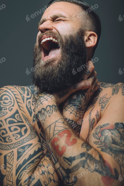 Preview: Portrait of young man with beard, covered in tattoos, hands around throat, screaming