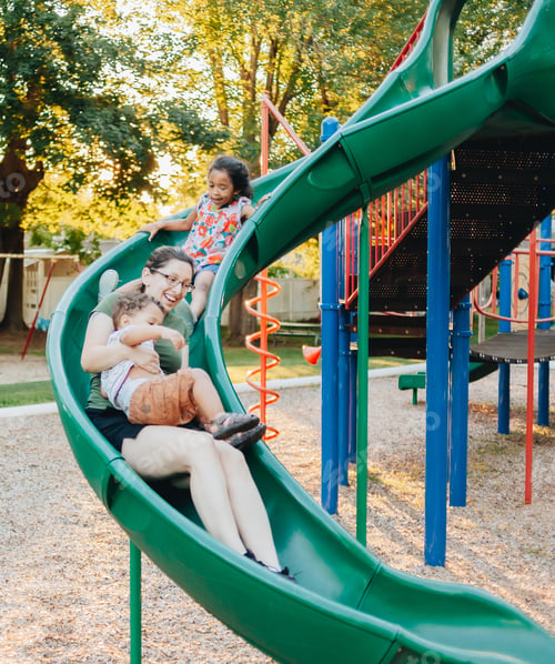 Preview: Young millennial mother at park with her two diverse children on a nice sunset summer day playscape
