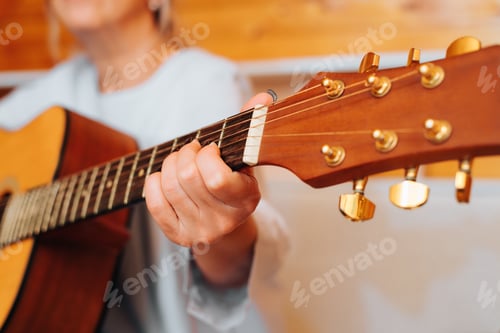 Preview: Close-up woman playing acoustic guitar while sitting indoors. Musician's female hand