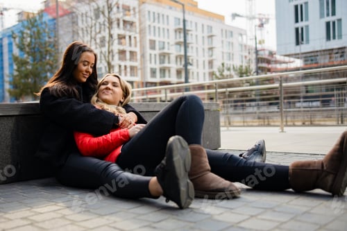 Preview: Happy Best Friends Embracing And Sitting On The Ground In City