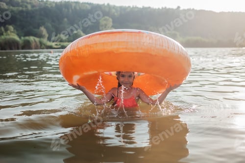 Preview: Girl has fun on big donut inflatable ring on lake on hot summer day, happy summertime, countryside
