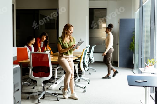 Preview: Young woman standing with digital tablet in front of her team at the office