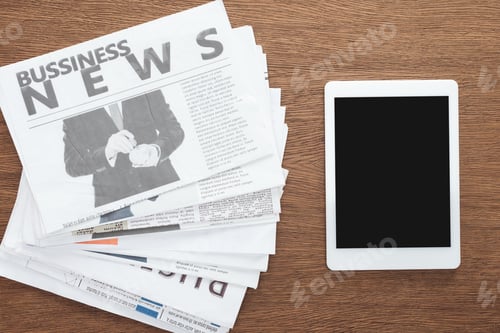 Preview: top view of tablet with blank screen and business newspapers on wooden tabletop