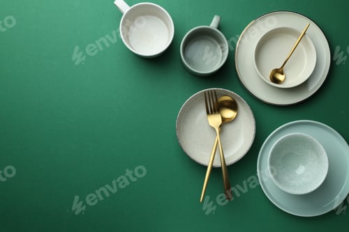 Preview: Stylish empty dishware and golden cutlery on green background, flat lay. Space for text